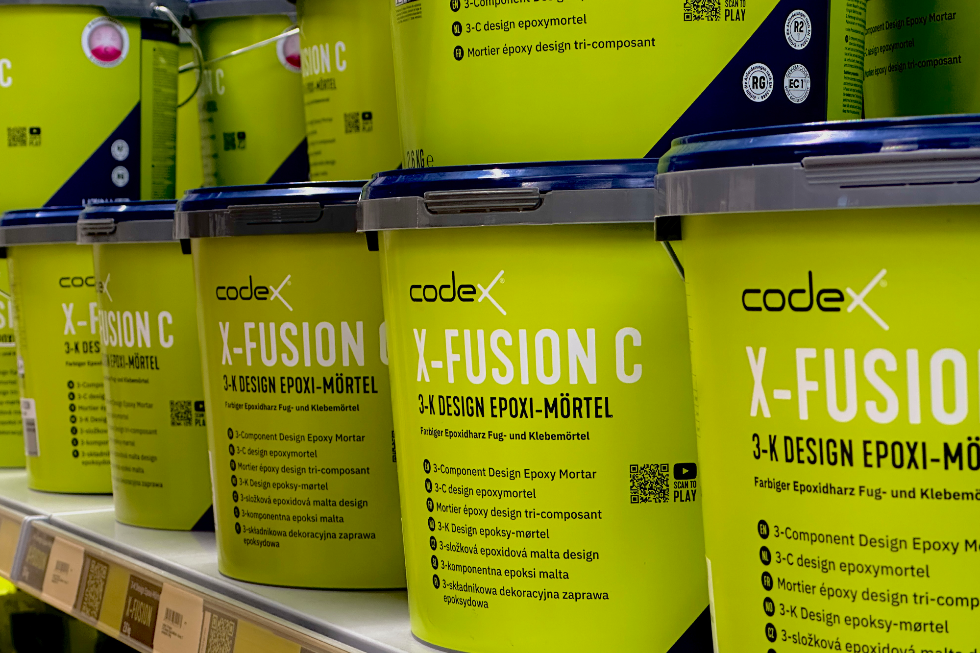 Mehrere hellgrüne Eimer des codex X-FUSION C 3-K Design Epoxi-Mörtels im Verkaufsregal bei Stolzenbach Baustoffe in Bremen.