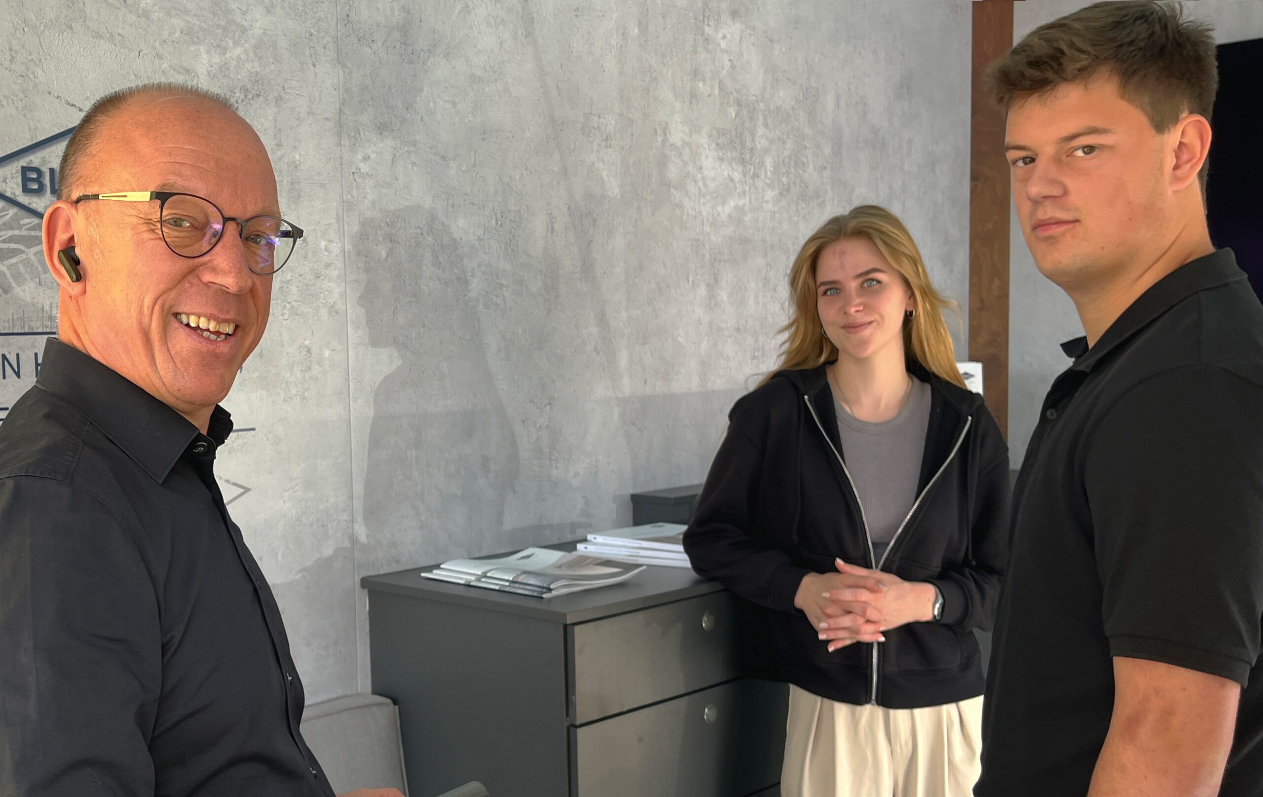 Drei Personen im Gespräch, darunter ein Mann mit Brille und zwei junge Erwachsene in einem modernen Raum.