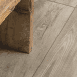 Nahaufnahme der Keramik-Terrassenplatte HAT-28 Grigio in grauer Holzoptik mit realistischer Maserung neben einem Holztisch.