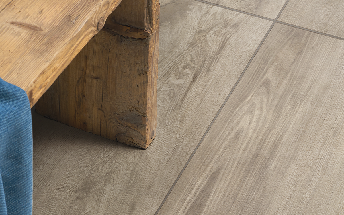 Nahaufnahme der Keramik-Terrassenplatte HAT-28 Grigio in grauer Holzoptik mit realistischer Maserung neben einem Holztisch.