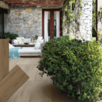 Terrasse mit Keramik-Bodenplatten in satter, brauner Holzoptik (Farbe Brown), kombiniert mit einer Natursteinwand und Lounge-Möbeln. Im Vordergrund drei Produktmuster der Serie HAT-87.